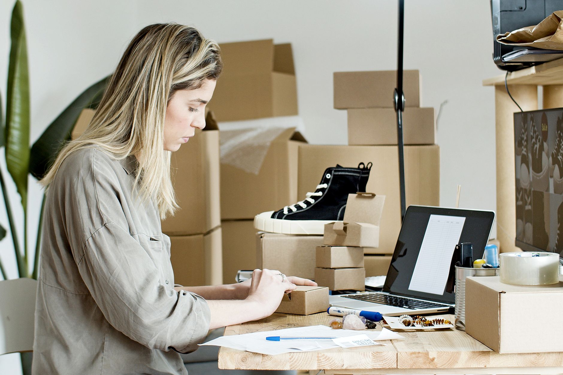 Mujer empaquetando cajas para su tienda online, con material de embalaje y un portátil al lado.